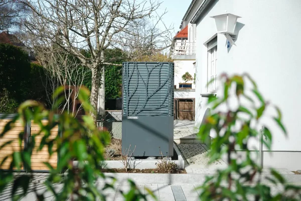 Außeneinheit einer Wärmepumpe mit Blende zwischen Sträuchern