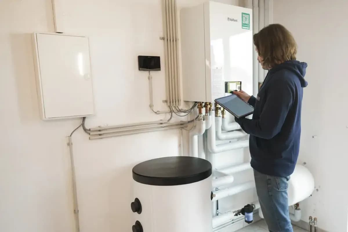 Technikraum mit Speicher und Hydraulik, Technikerin prüft am Tablet